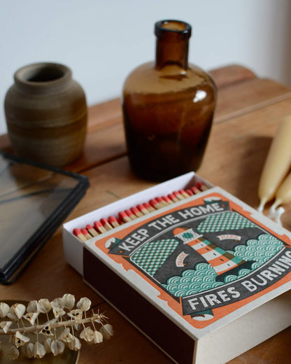 An orange and green letterpress design match box, next to vases and candles.