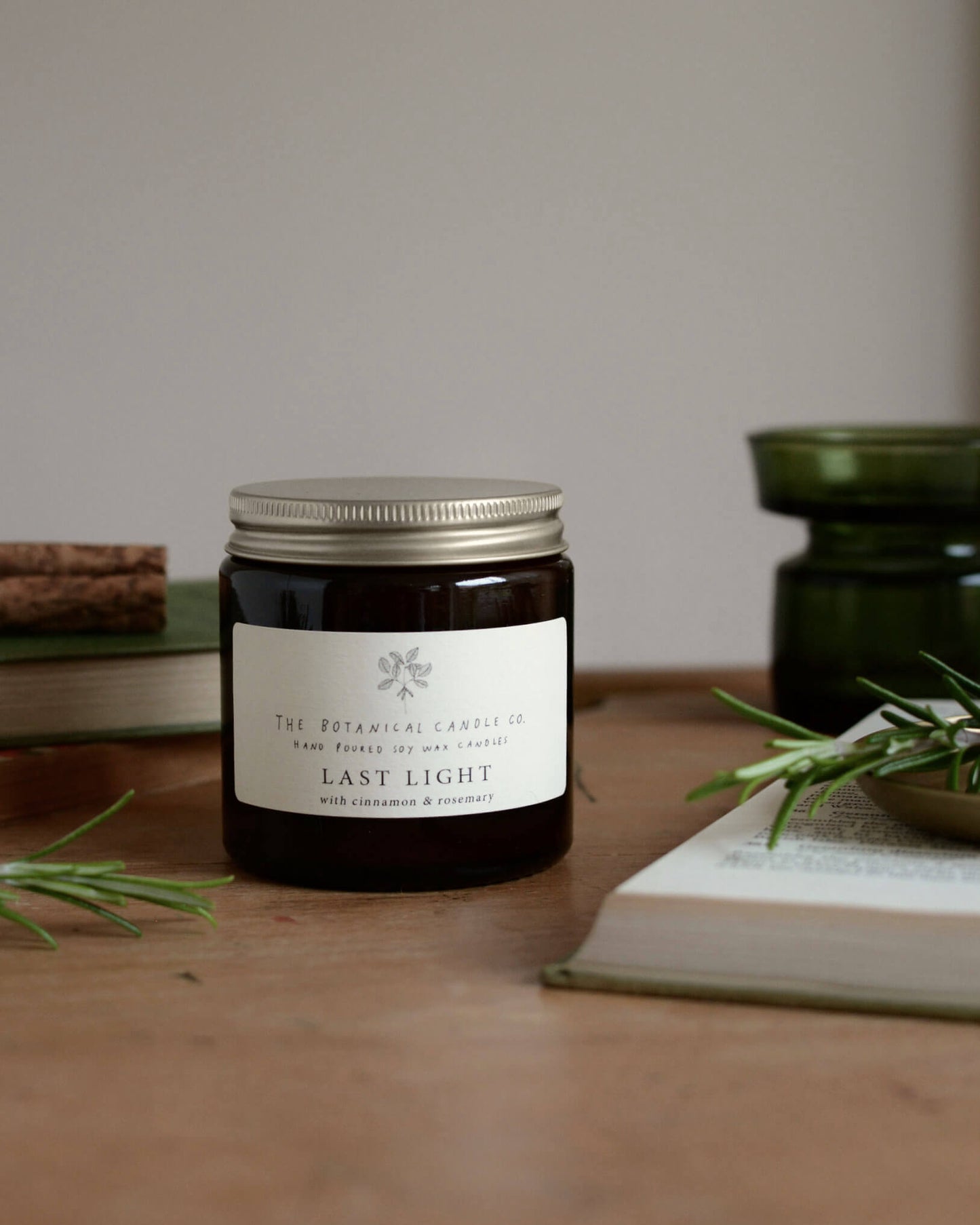 A 120ml Christmas blend scented candle in an amber glass jar, surrounded by rosemary sprigs and cinnamon sticks.