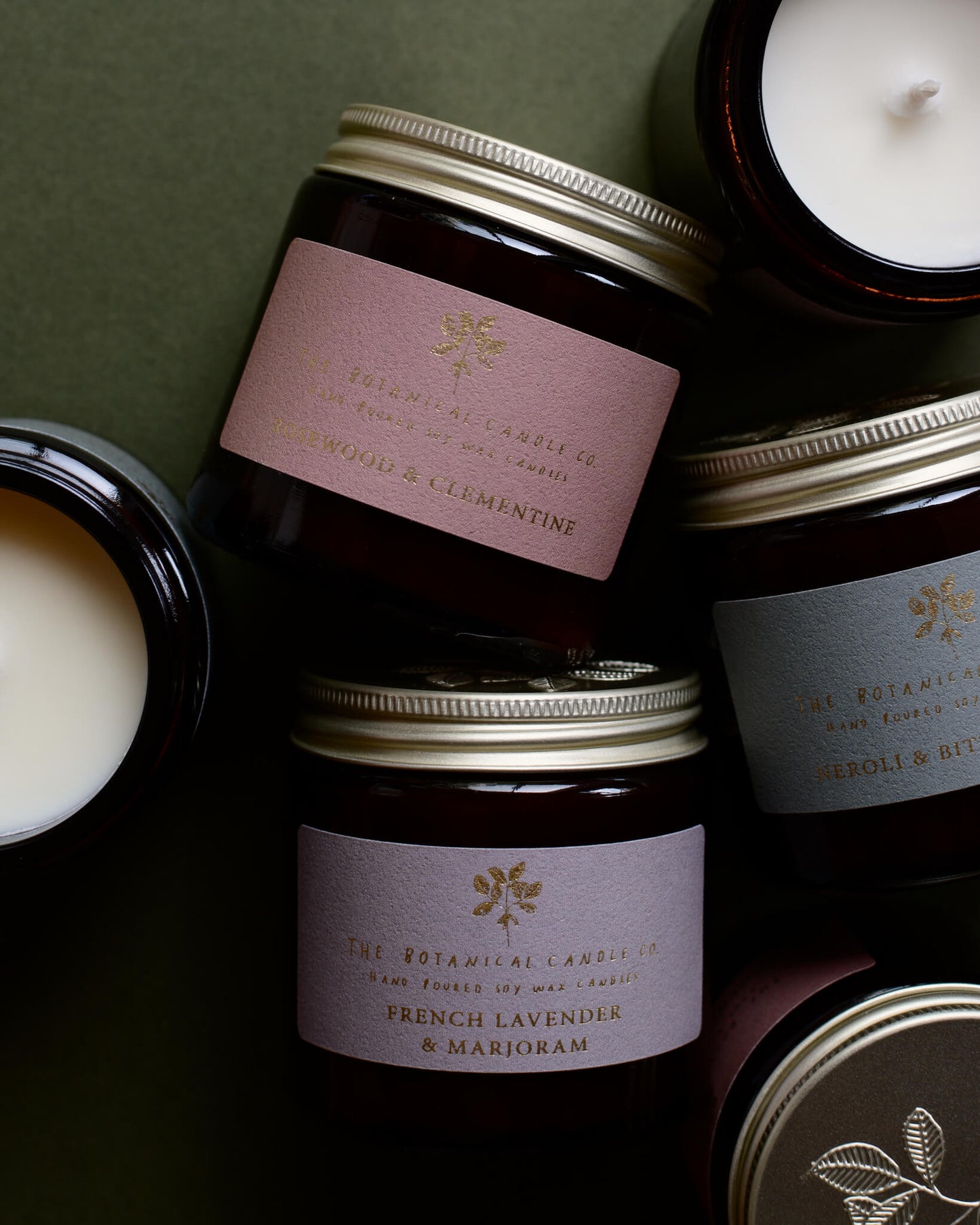 Collection of scented candles in amber glass jars, on a green background.