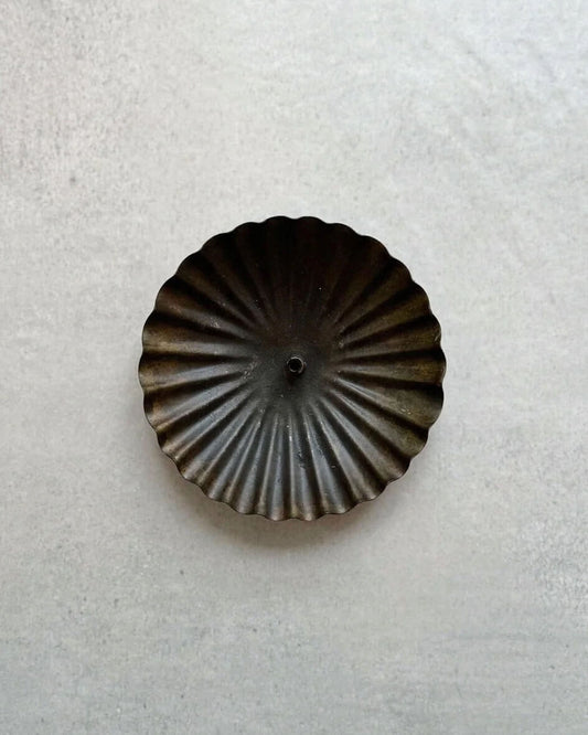 A metal incense holder in a fluted circle design, with a bronzed finish.