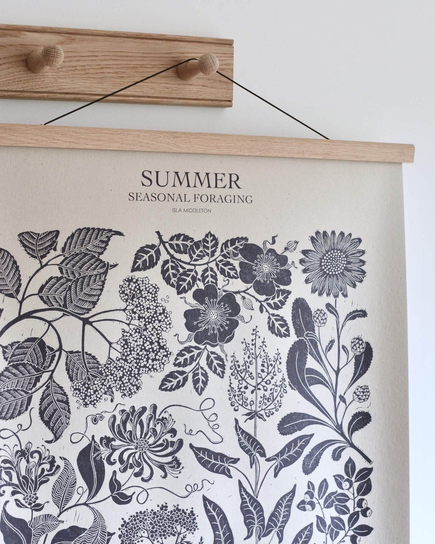 A poster depicting Summer plants, displayed on an oak shaker peg rail with 2 pegs.