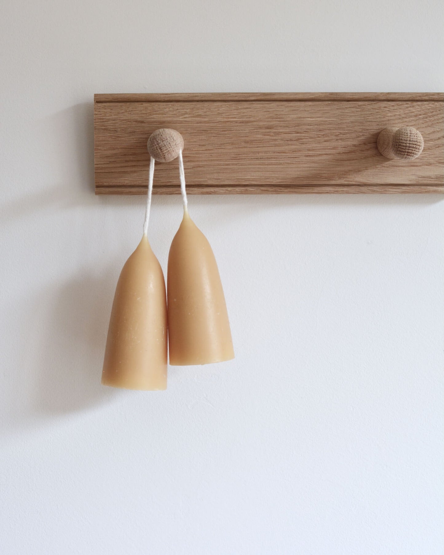 A pair of stubby beeswax candles, displayed on an oak shaker peg rail.