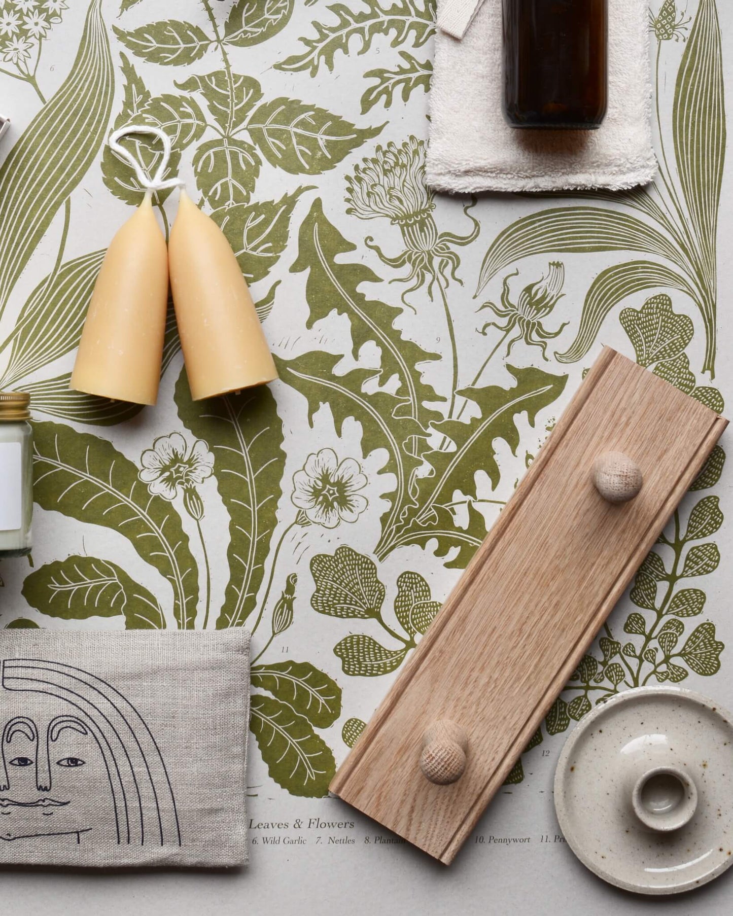 An oak shaker peg rail and beeswax candles, displayed on top of a green botanical print.