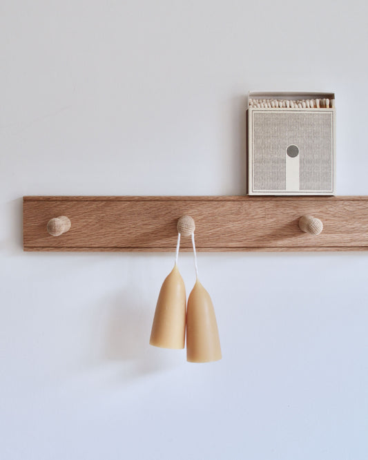 A solid oak peg rail, displaying beeswax candles and a box of matches.