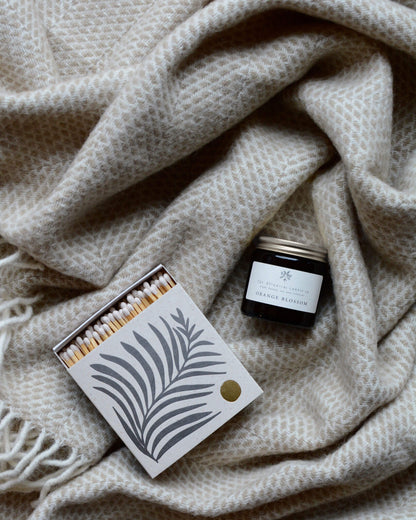 Orange Blossom scented soy wax candle by The Botanical Candle Co. on a woollen blanket with a box of matches.