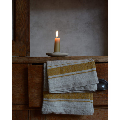 A styled image of a ceramic candle holder with a beeswax candle with flame on a wooden cabinet.