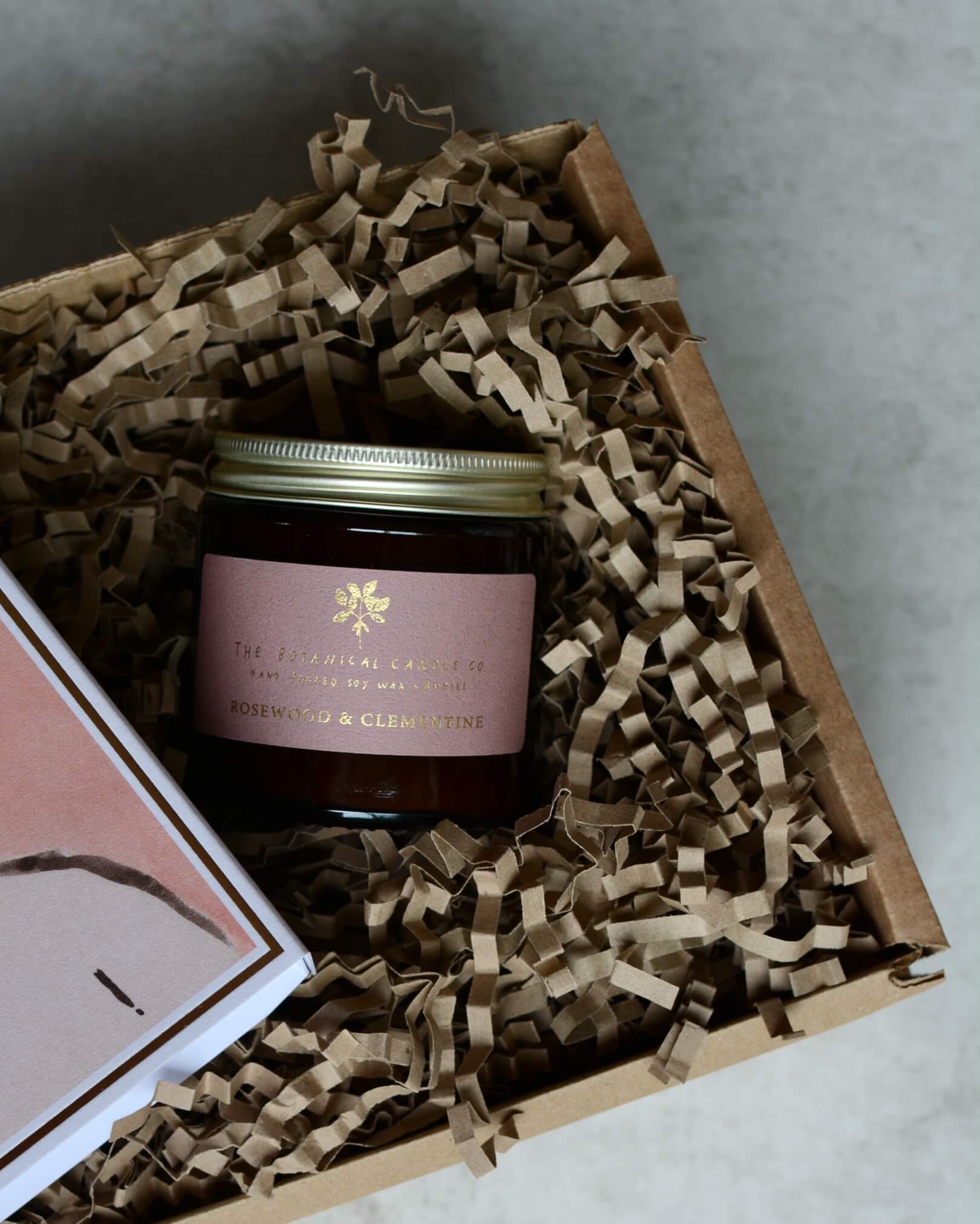 A gift box containing a pink rose candle and a pink and white illustrated box of matches.