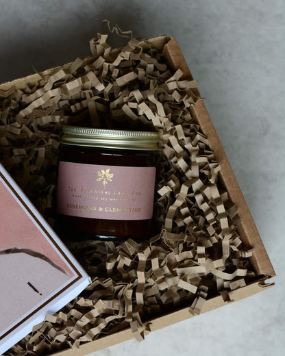 A gift box containing a pink rose candle and a pink and white illustrated box of matches.