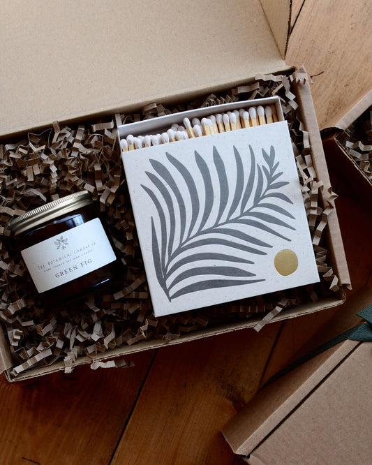 A gift box containing a glass jar candle and a box of letterpress matches.