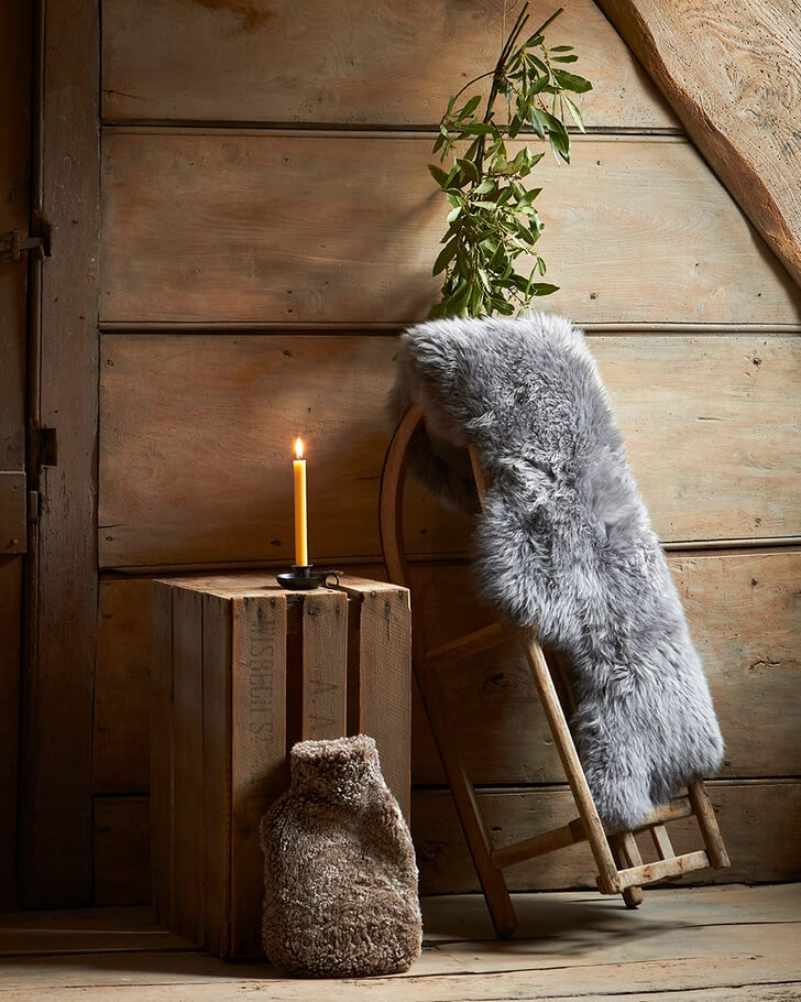 A brown sheepskin hot water bottle next to a lit candle and a sheepskin rug.