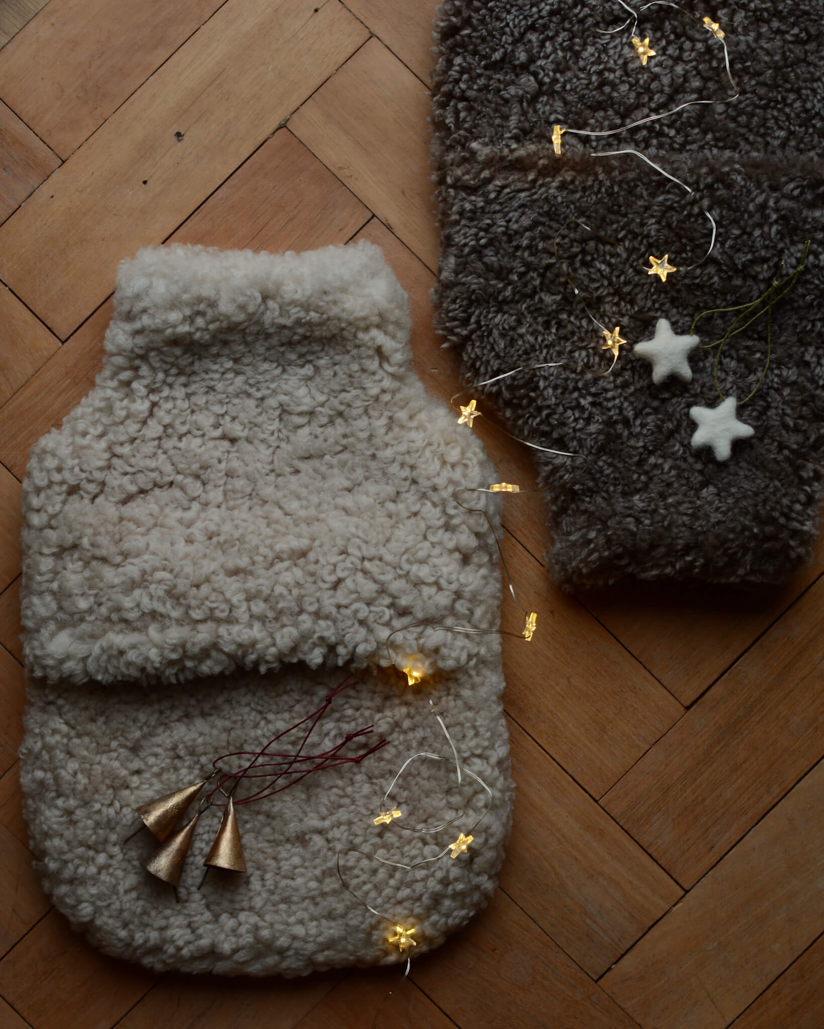 A brown sheepskin hot water bottle next to a natural sheepskin hot water bottle, with twinkly Christmas lights.