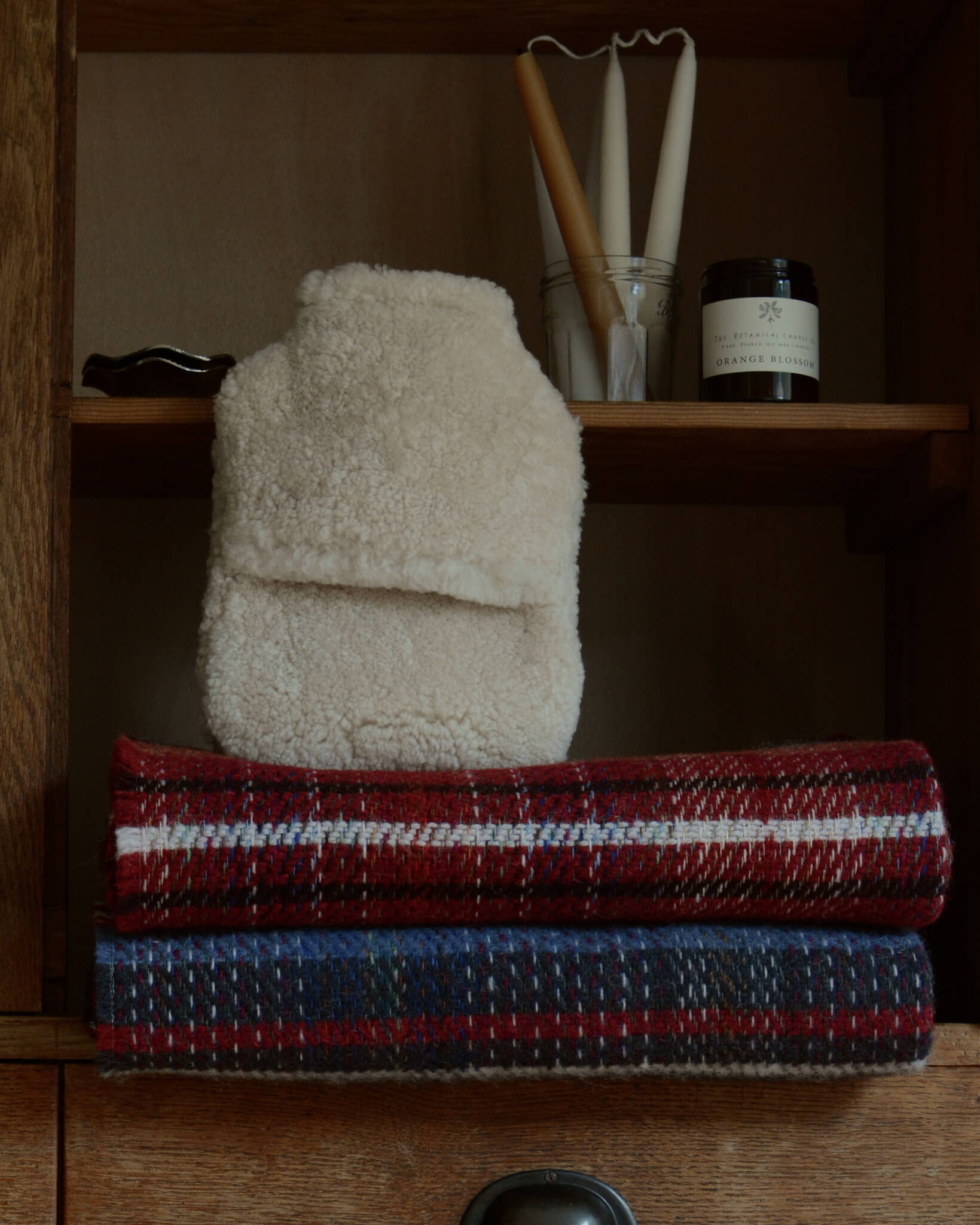 A natural sheepskin hot water bottle on top of some checked wool blankets.