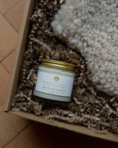 A natural sheepskin hot water bottle next to a candle in a gift box.