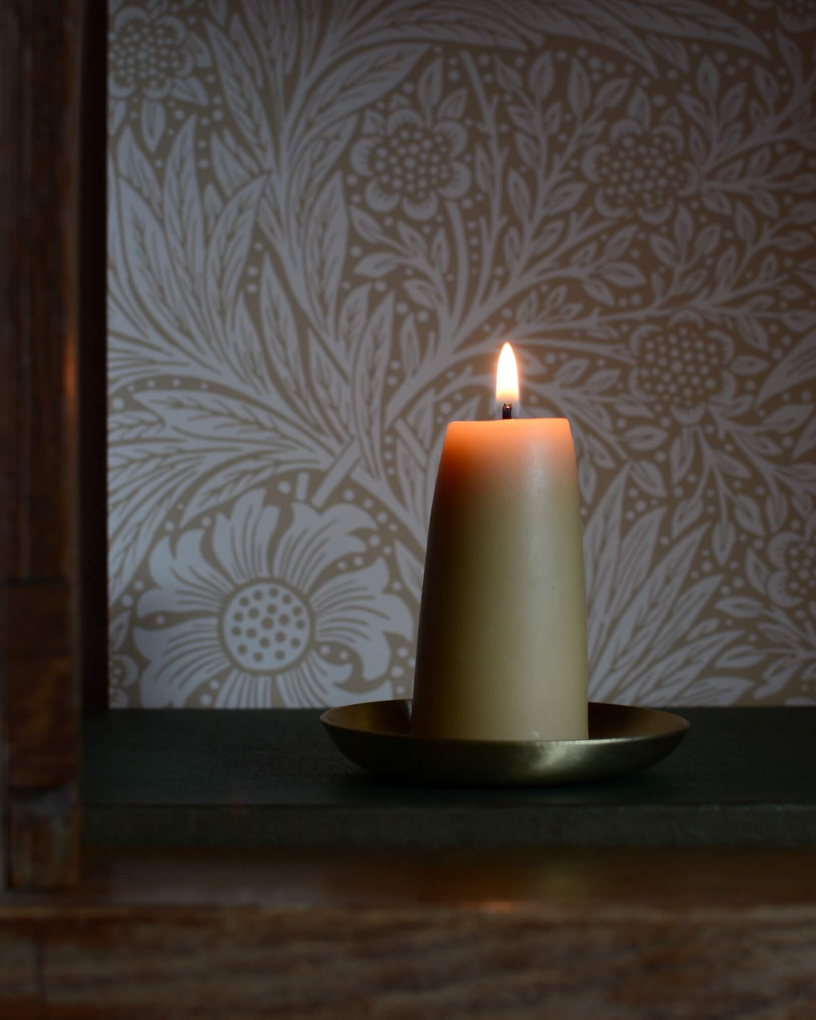 A solid brass candle dish, with a lit beeswax candle.