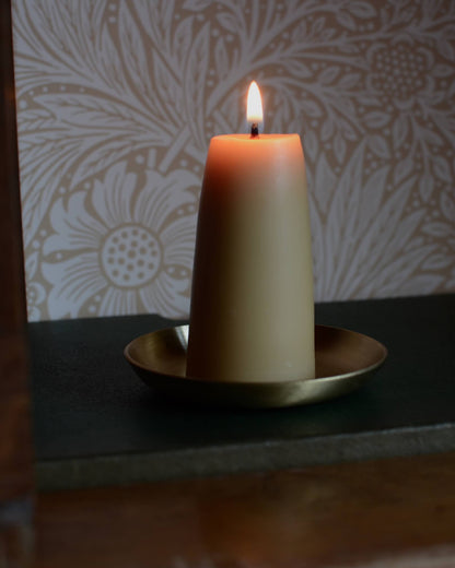 A solid brass candle dish, with a lit beeswax candle.