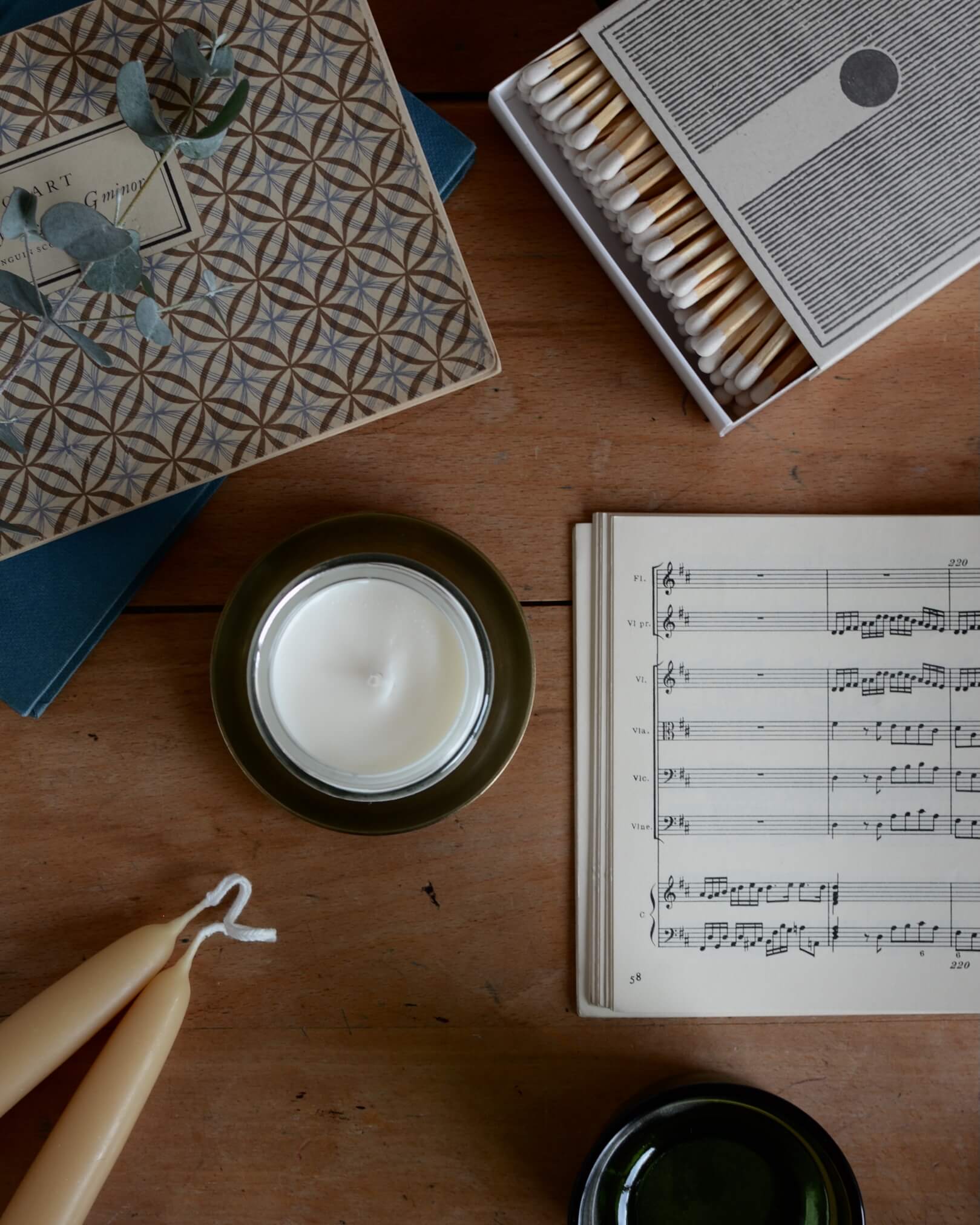 A jar candle on top of a brass candle dish, surrounded by beeswax candles, matches and other homewares.