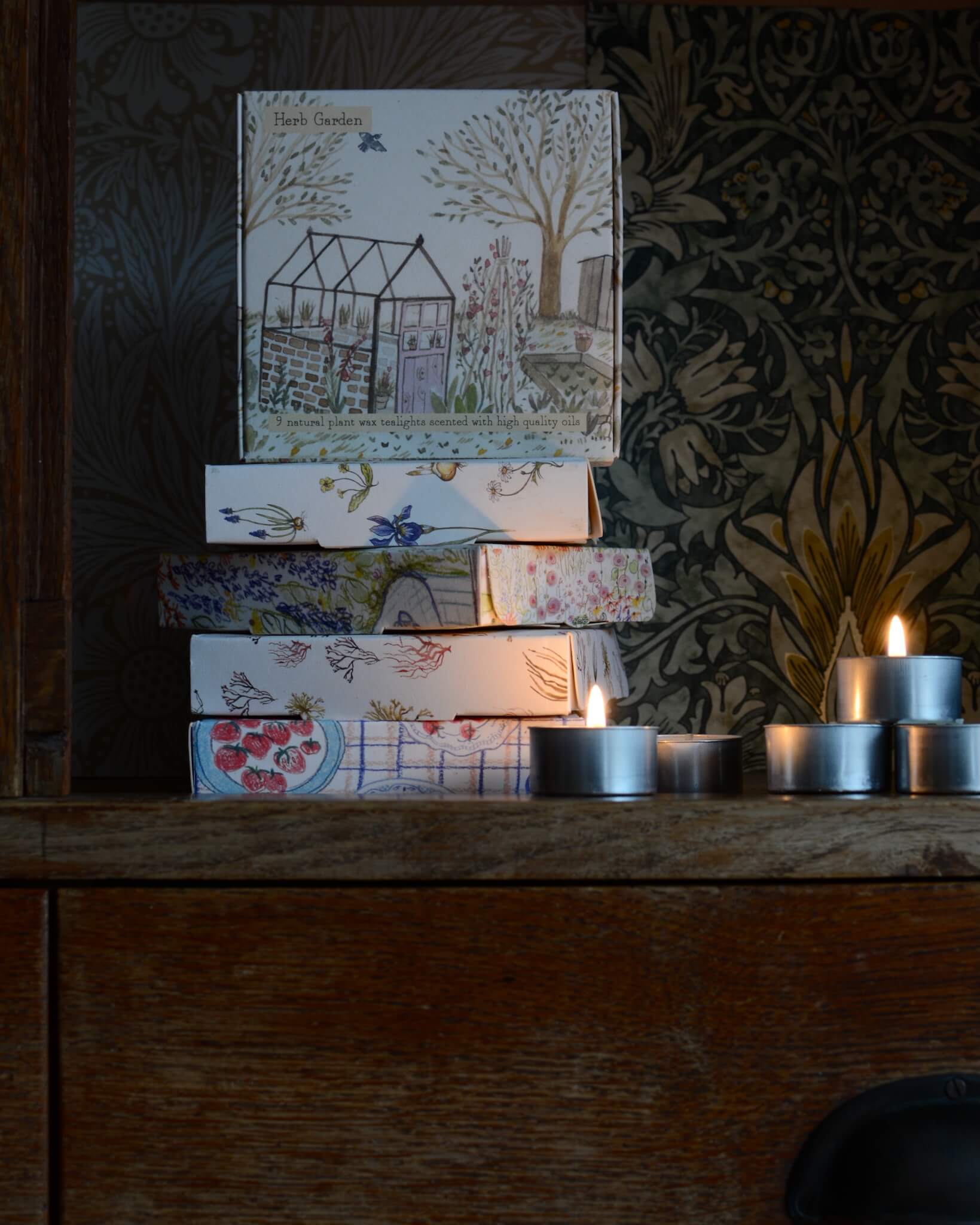 A box of tealights, with an illustrated box featuring a glasshouse within a summer garden.