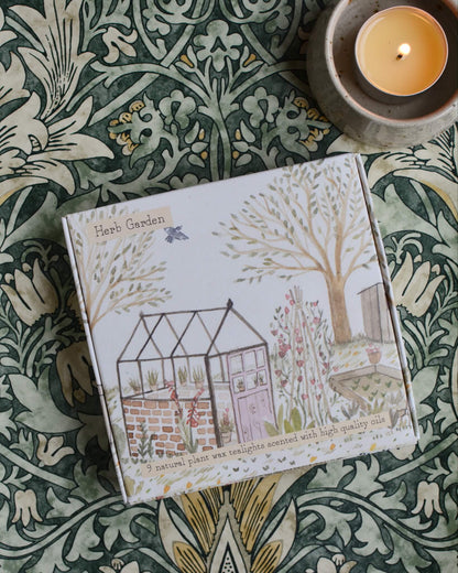 A box of tealights, with an illustrated box featuring a glasshouse within a summer garden.