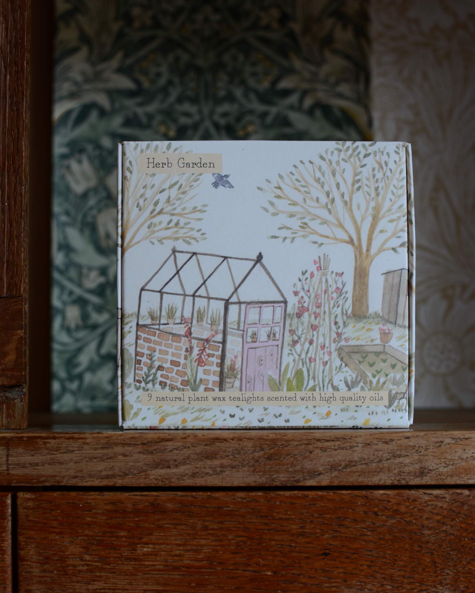 A box of tealights, with an illustrated box featuring a glasshouse within a summer garden.