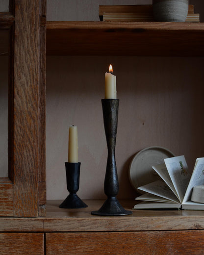 A pair of tall metal black candlesticks, forged from iron.