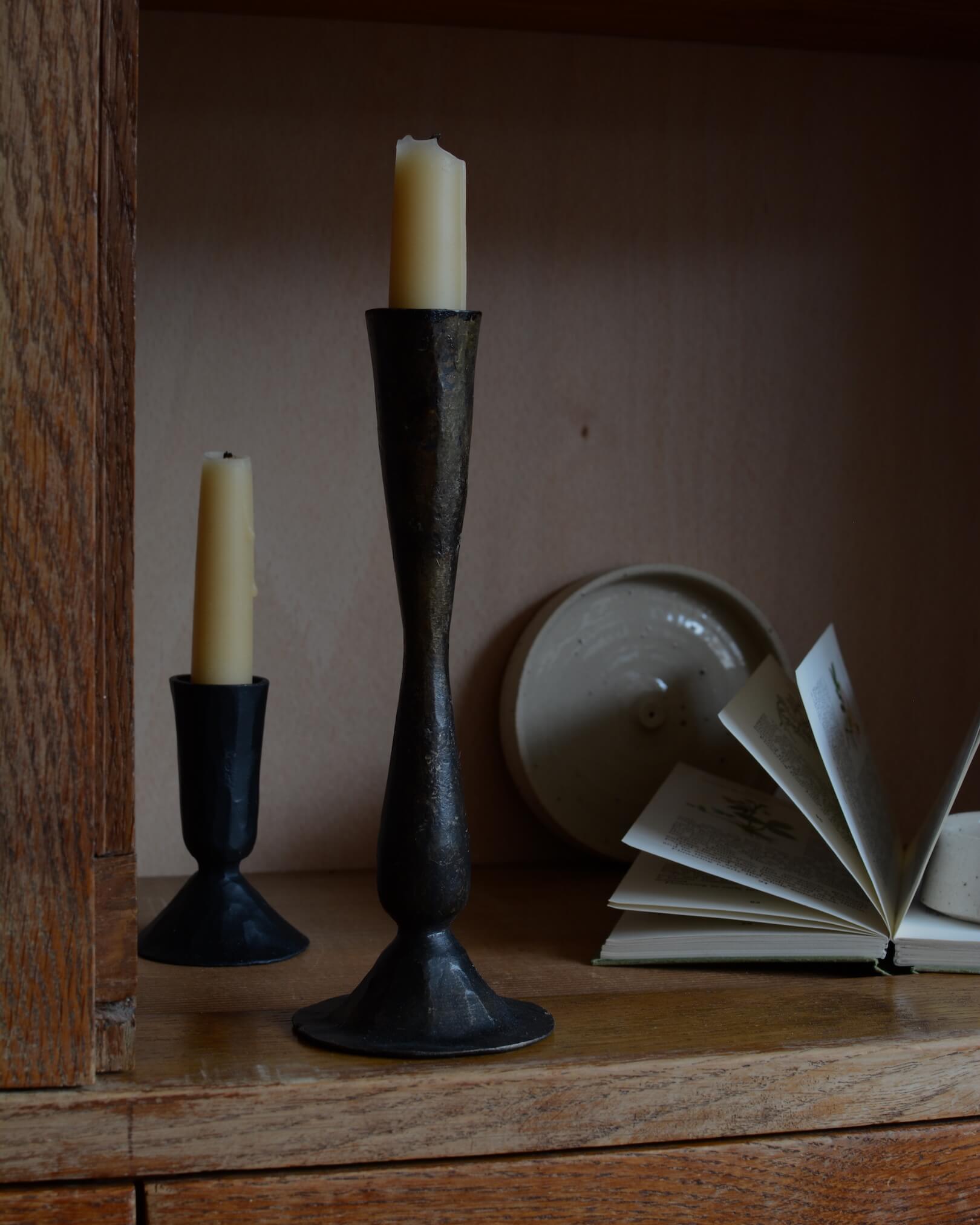 A pair of tall metal black candlesticks, forged from iron.