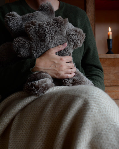 A seated woman hugging teddy bear sheepskin hot water bottles.