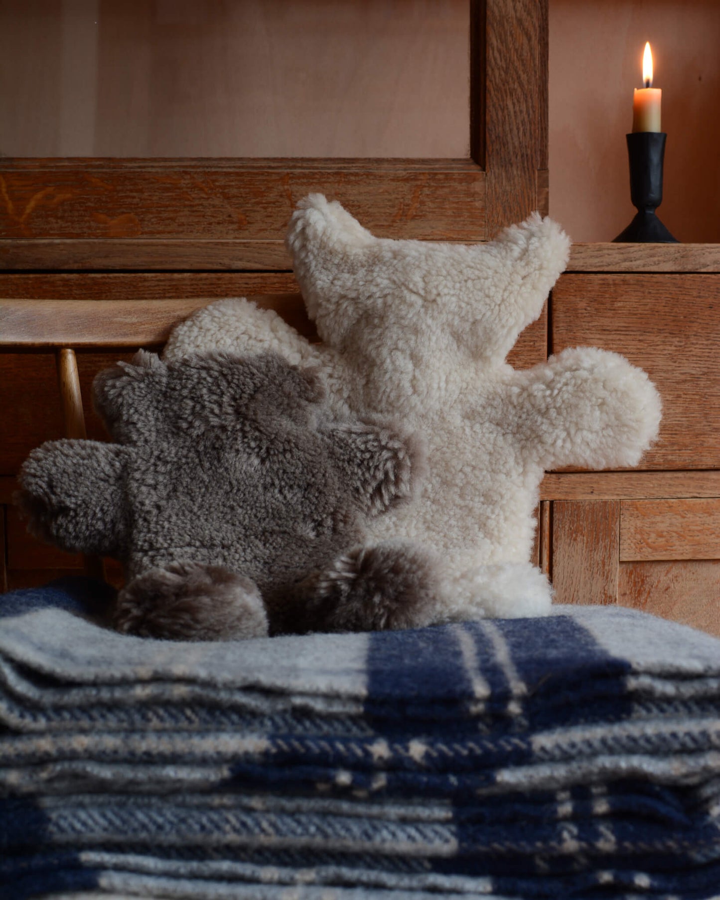 A pair of teddy bear sheepskin hot water bottles, on top of a checked wool blanket.