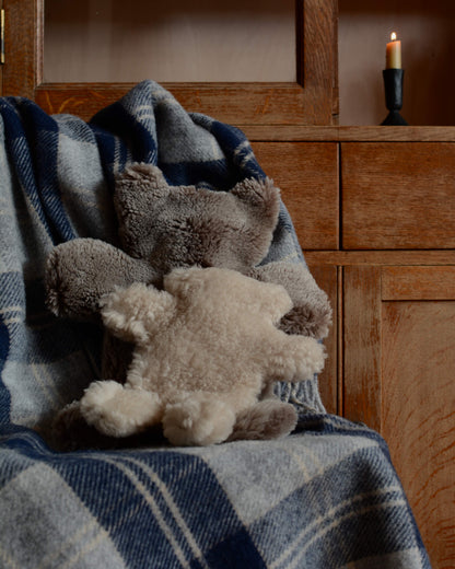 Teddy bear sheepskin hot water bottles on top of a woollen blanket.