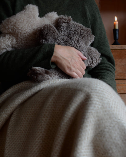 A seated woman hugging teddy bear sheepskin hot water bottles.