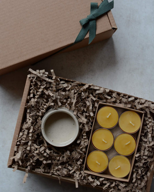 A gift box containing beeswax tealights and a ceramic tealight holder.