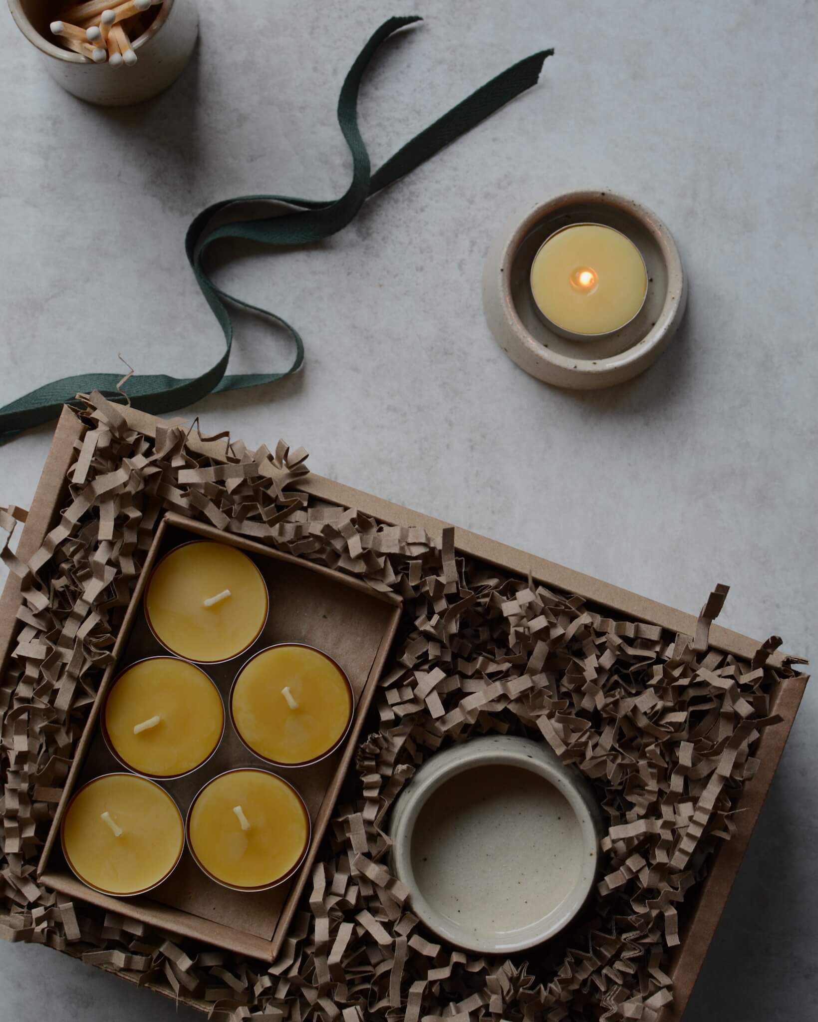 A gift box containing beeswax tealights and a ceramic tealight holder.