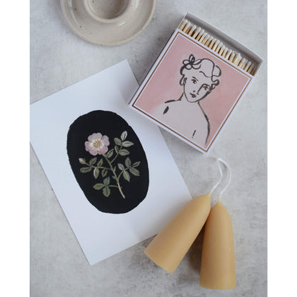 Pink matchbox alongside a floral rose illustration and beeswax candles.