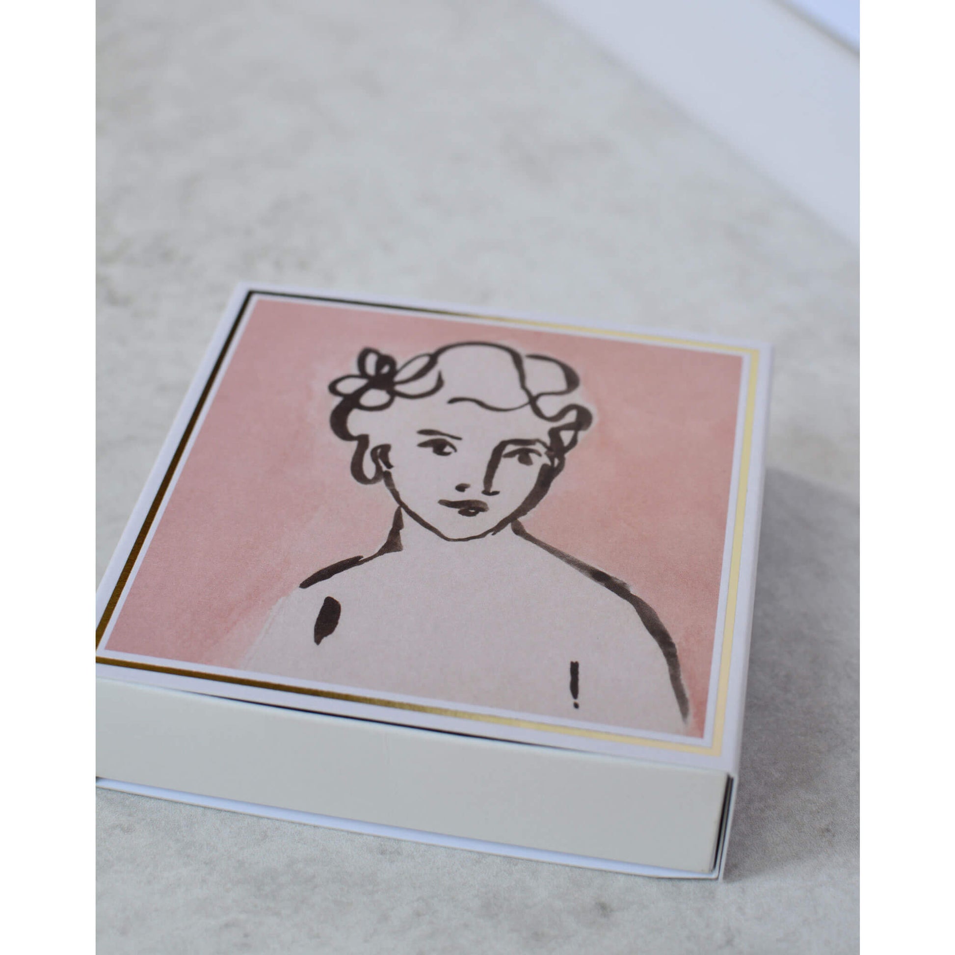 Square matchbox featuring an illustration of a woman on a pink background.