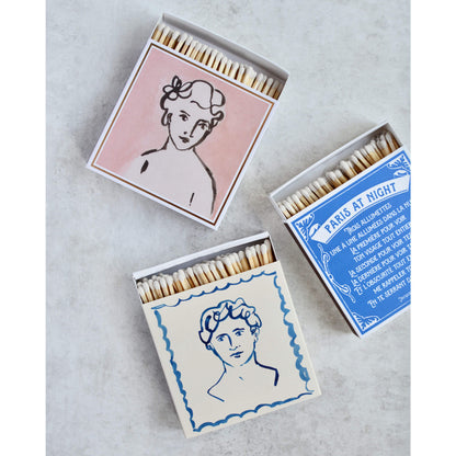 Square match boxes with portrait designs on a marble stone background.