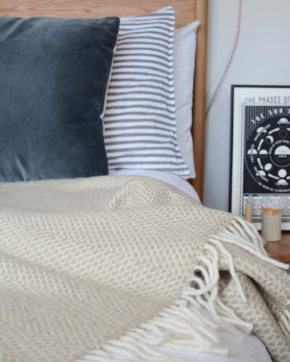 An oatmeal beehive pattern blanket, draped across a bed, with blue pillows.