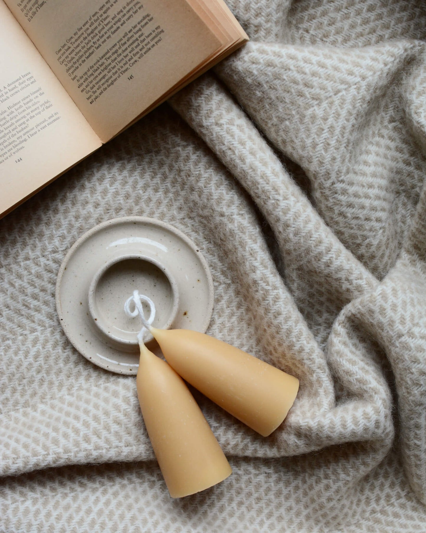 An oatmeal beehive pattern blanket, with a book, candle holder and candle on top.