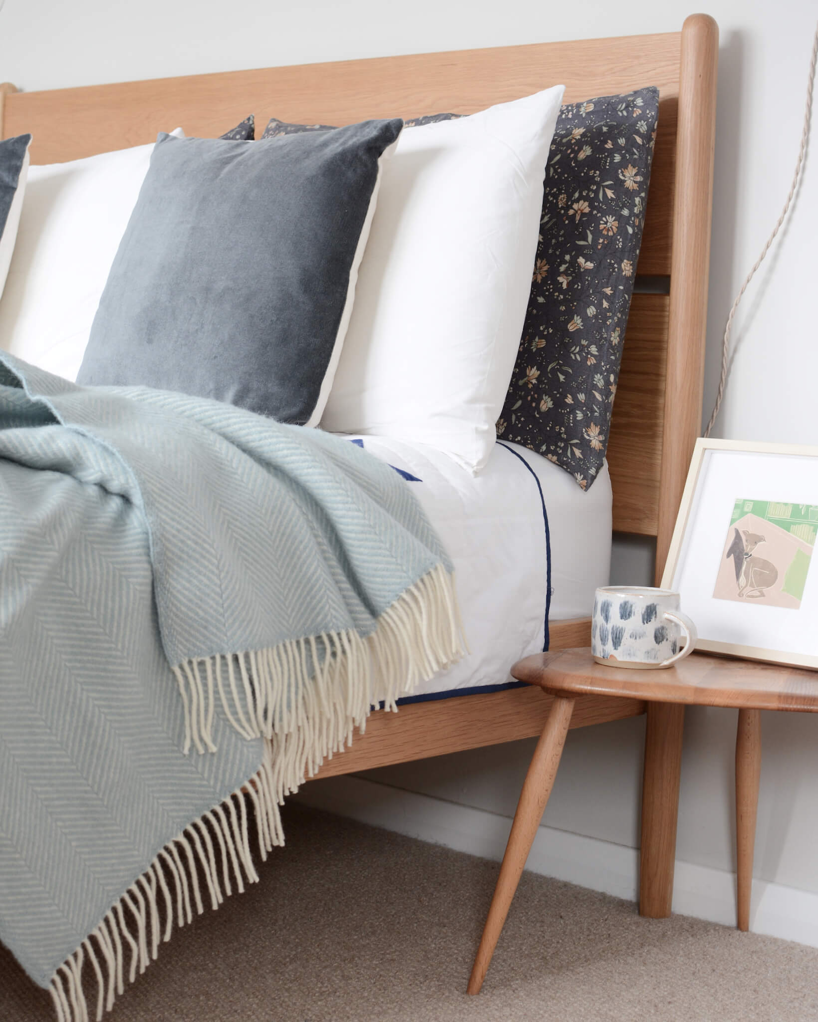 A duck egg herringbone weave blanket, on a wooden bed, with pillows.