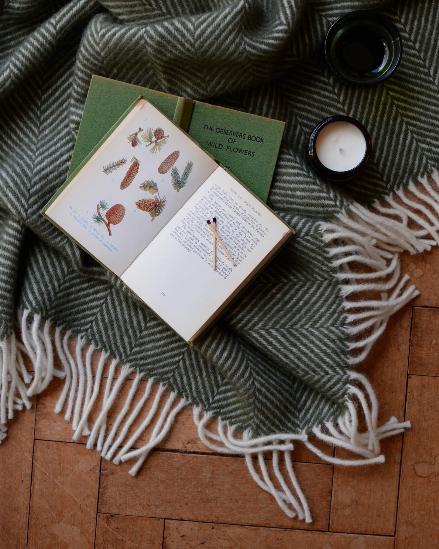 A green woollen herringbone blanket with books and candles on top.