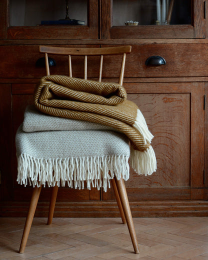 A mustard yellow wool herringbone blanket and oatmeal blanket on a wooden chair.