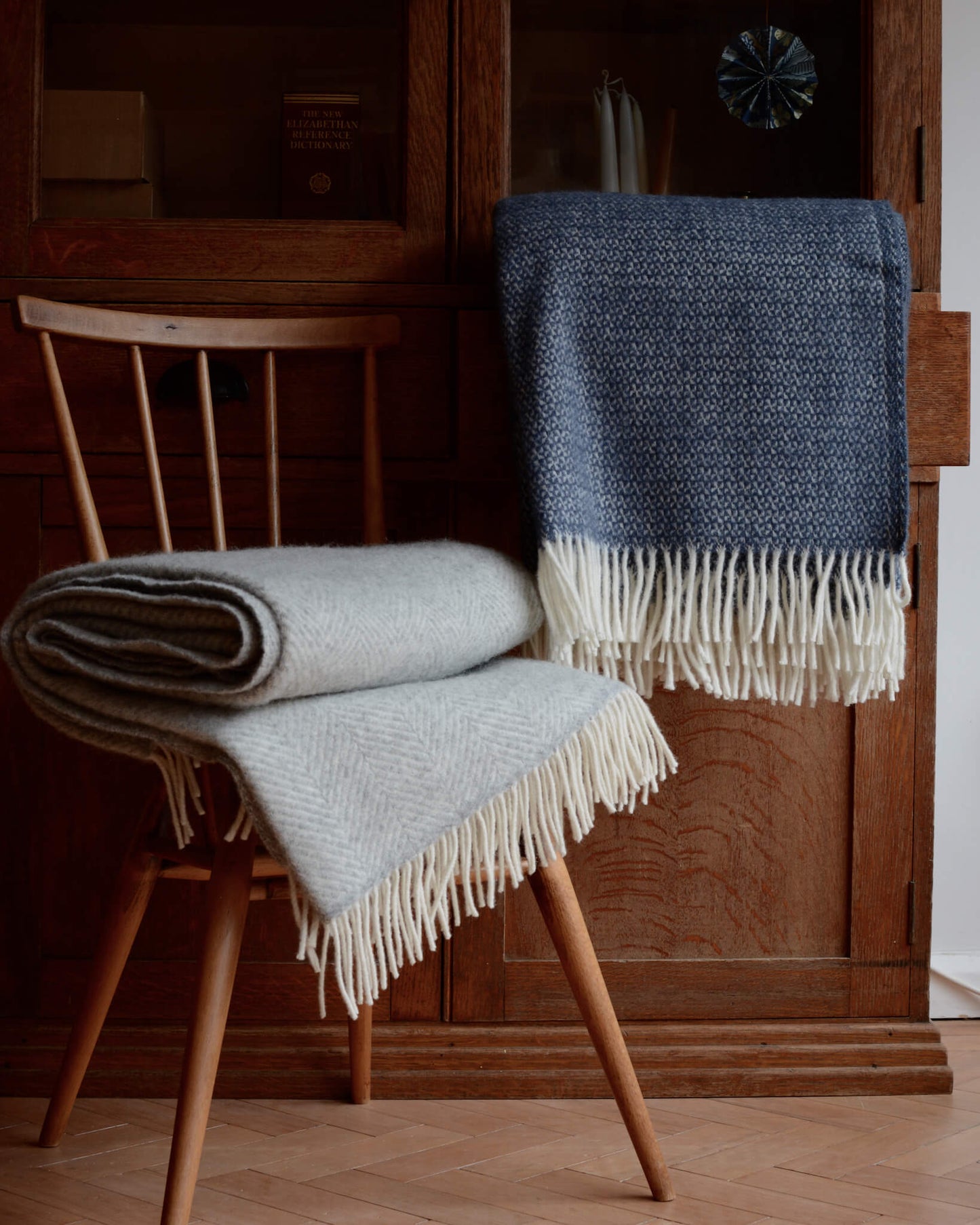 Blue and grey wool blankets, in front of a wooden cabinet.