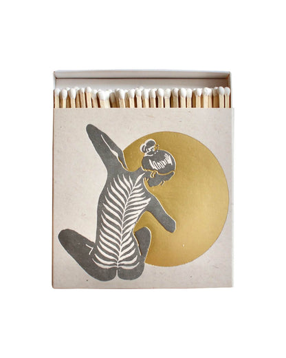 A white match box featuring a yoga figure in front of a shiny gold moon. 