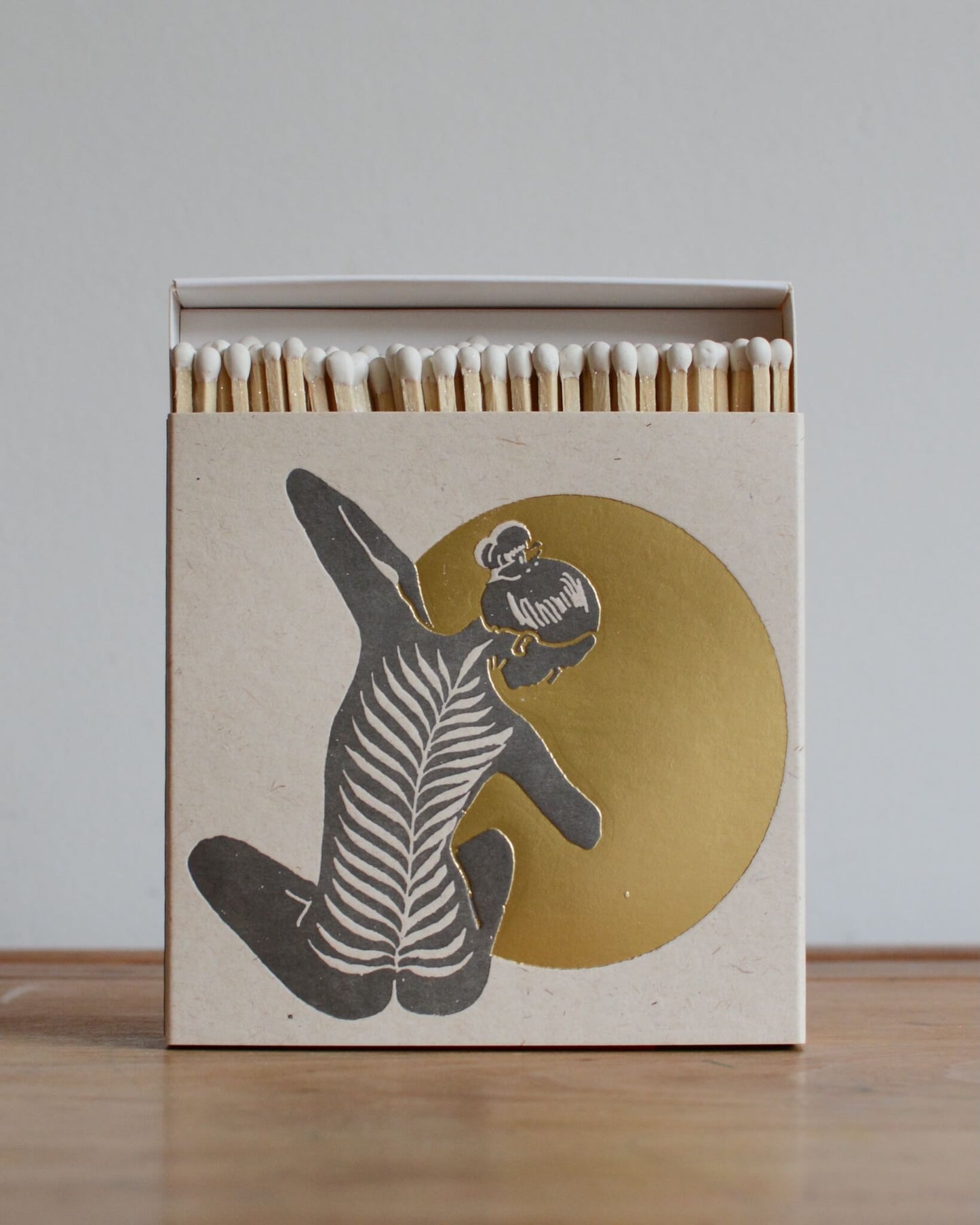 A white match box featuring a yoga figure in front of a shiny gold moon. 