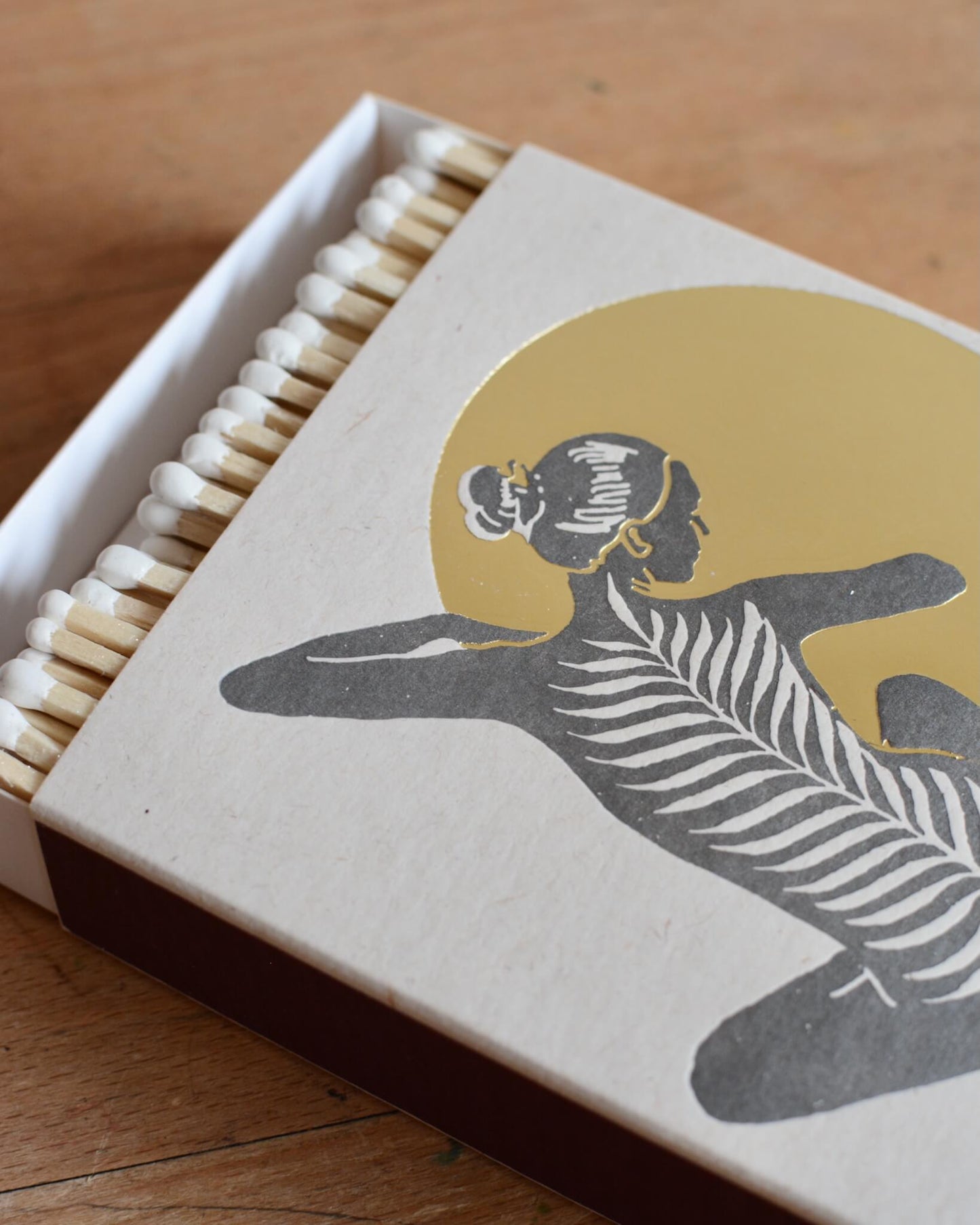 A close-up of a white match box featuring a yoga figure in front of a shiny gold moon. 