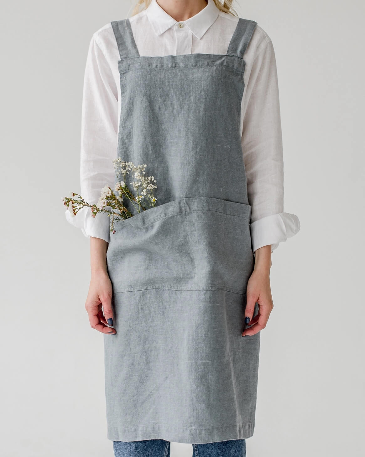 A linen cross back apron in a soft, grey blue, shown on a model.