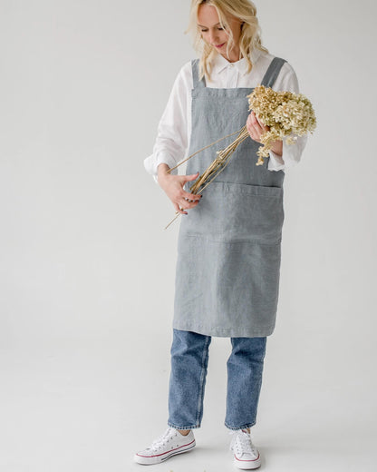 A linen cross back apron in a soft, grey blue, shown on a model.