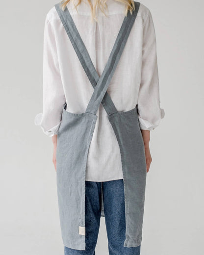 The back of a linen cross back apron in a soft, grey blue, shown on a model.