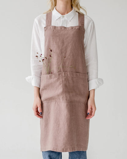 A linen cross back apron in a dusky soft pink, shown on a model.