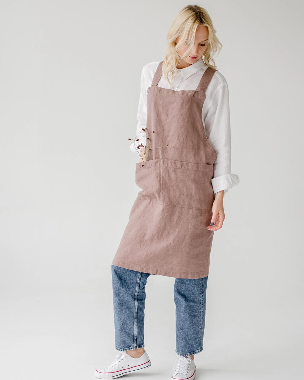 A linen cross back apron in a dusky soft pink, shown on a model.