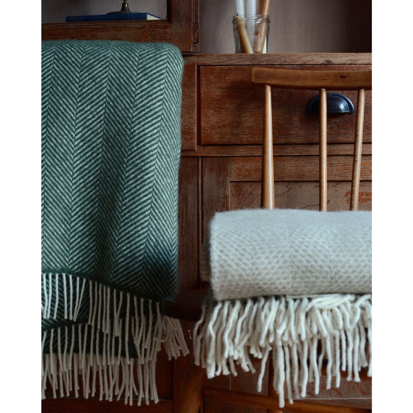 Detail shot of an olive green Tweedmill herringbone wool throw, shown next to an oatmeal throw on top of a chair.