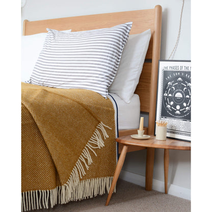 Mustard yellow wool blanket with an ivory fringe, draped across a bed.